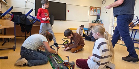 Powiększ grafikę: Uczniowie układają tory z klocków w sali lekcyjnej.