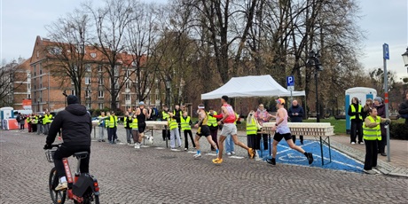 Powiększ grafikę: Biegacze oraz wolontariusze podczas podawania napojów na trasie maratonu.