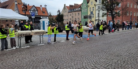 Powiększ grafikę: Biegacze oraz wolontariusze podczas podawania napojów na trasie maratonu.