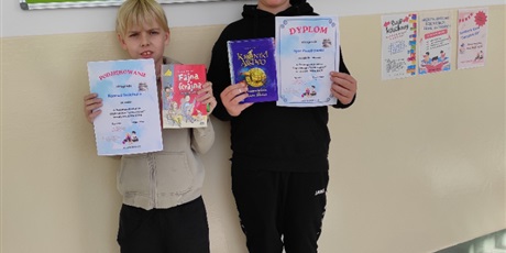 Powiększ grafikę: Uczniowie z dyplomami i nagrodami za konkurs czytelniczy  na korytarzu szkolnym.