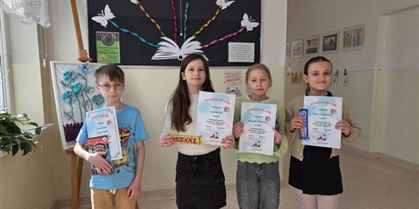 Powiększ grafikę: Uczniowie z dyplomami i nagrodami za konkurs czytelniczy na korytarzu szkolnym.