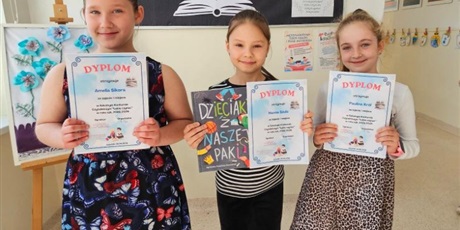 Powiększ grafikę: Uczennice z dyplomami i nagrodami za konkurs czytelniczy  na korytarzu szkolnym.
