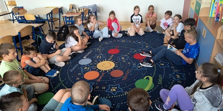 Powiększ grafikę: Uczniowie siedzą w kole na dywanie w sali lekcyjnej i czytają książki.