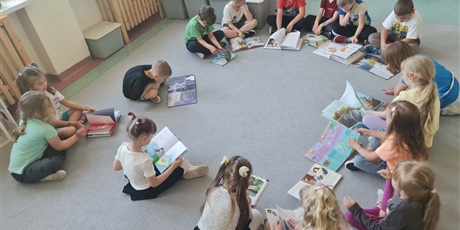 Powiększ grafikę: Uczniowie siedzą w kole na dywanie w sali lekcyjnej i czytają książki.
