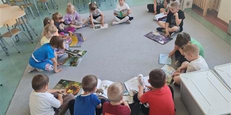 Powiększ grafikę: Uczniowie siedzą w kole na dywanie w sali lekcyjnej i czytają książki.
