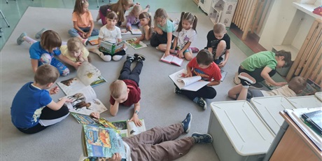 Powiększ grafikę: Uczniowie siedzą w kole na dywanie w sali lekcyjnej i czytają książki.