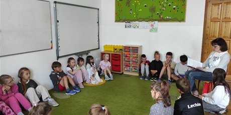Powiększ grafikę: Uczniowie siedzą w kole na dywanie w świetlicy, nauczyciel czyta książkę.