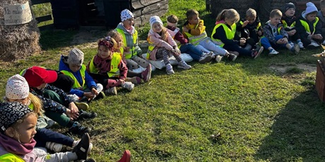 Powiększ grafikę: Zbiorowe zdjęcie uczniów siedzących w kole w zagrodzie wiejskiej podczas zajęć.