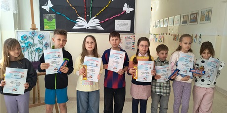 Powiększ grafikę: Uczniowie z dyplomami i nagrodami za konkurs czytelniczy na korytarzu szkolnym.